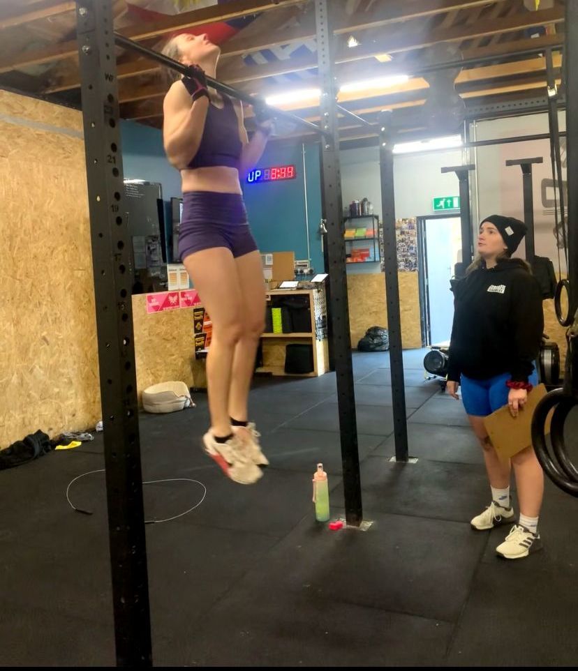 A woman is pulling up on a bar in a gym