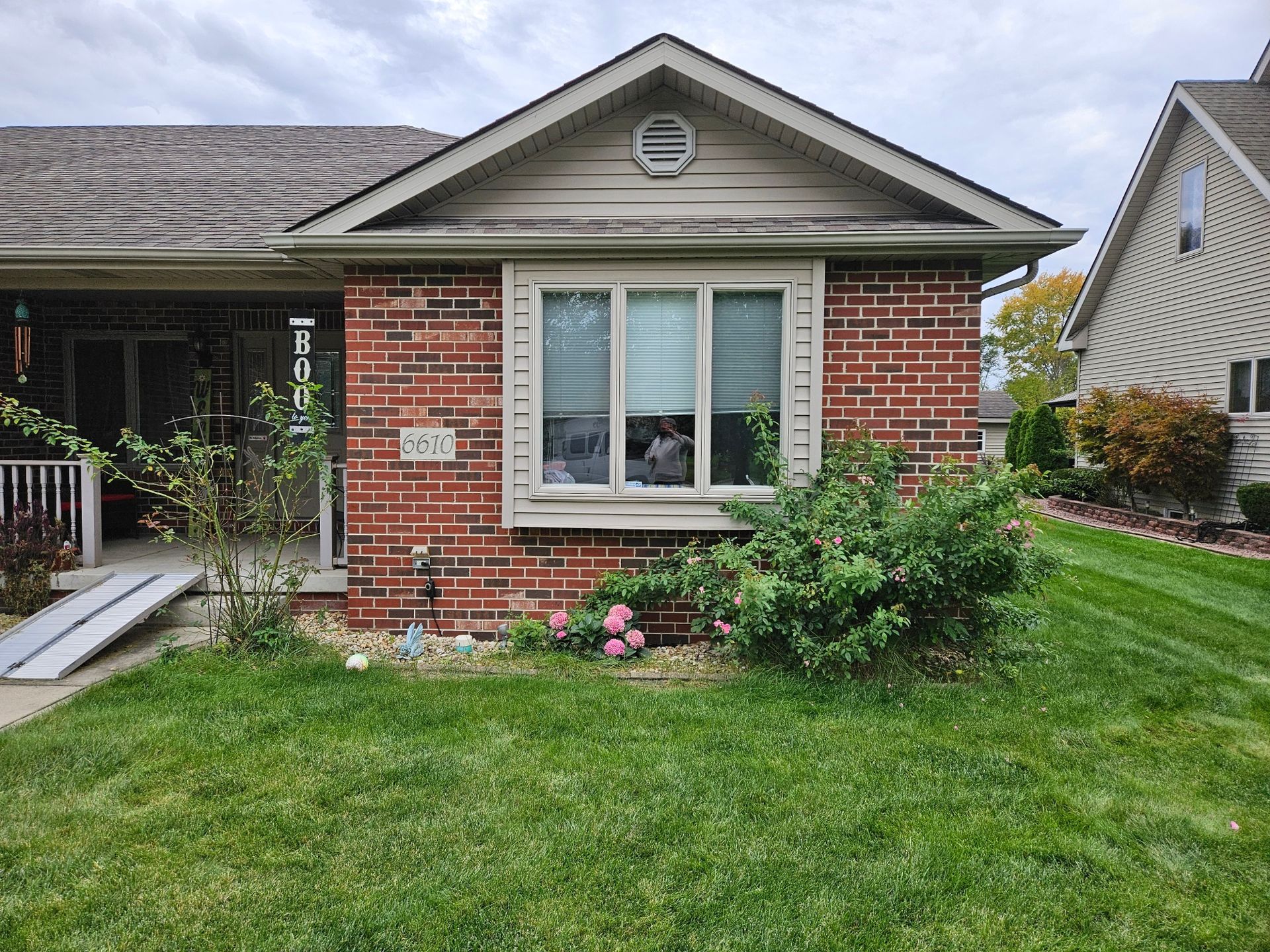 Front yard with a leafless tree, green grass, and a townhouse exterior with a patio and small garden beds.