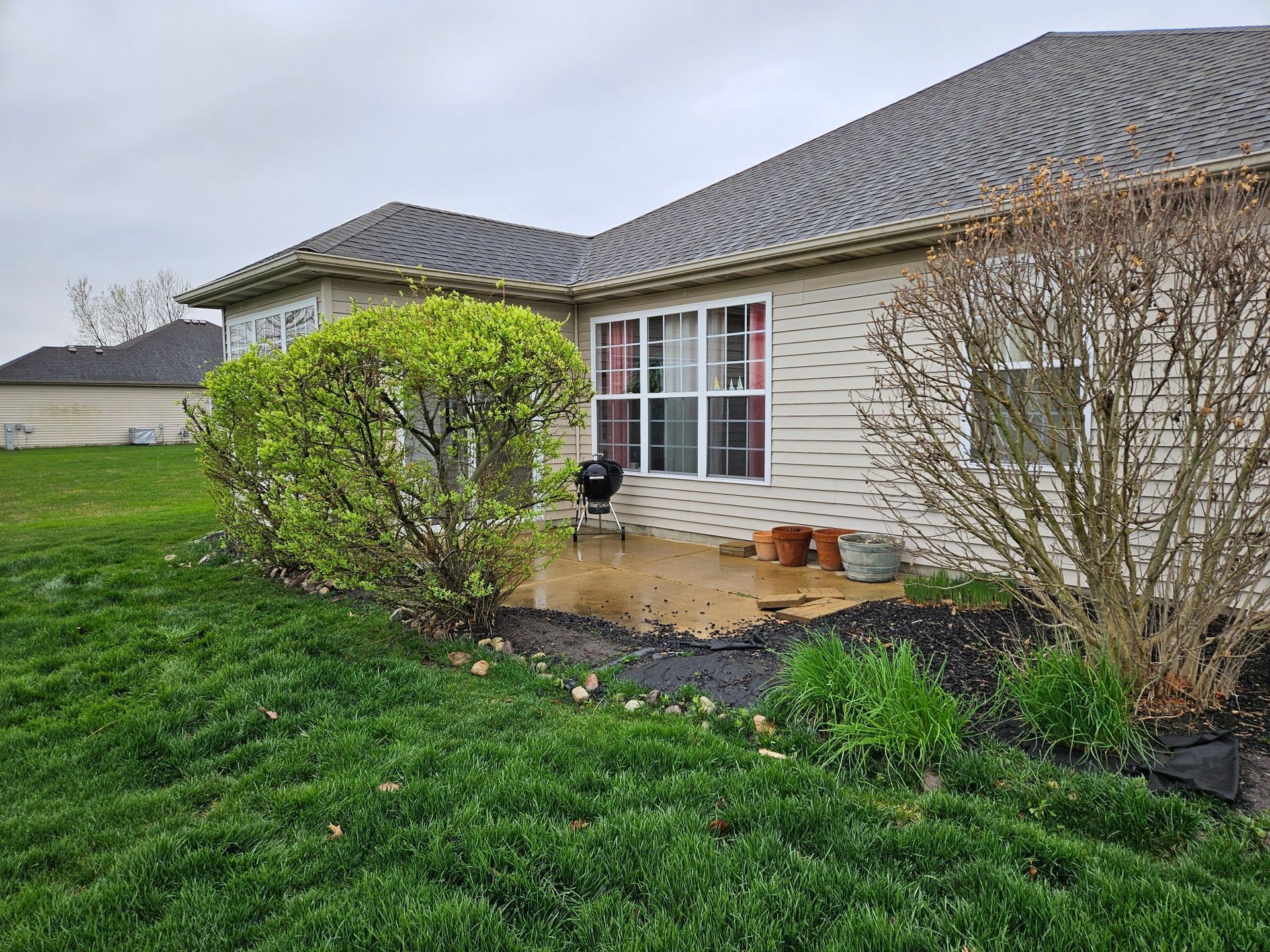 Suburban house patio with sliding glass doors, green lawn, and shrubs in front.