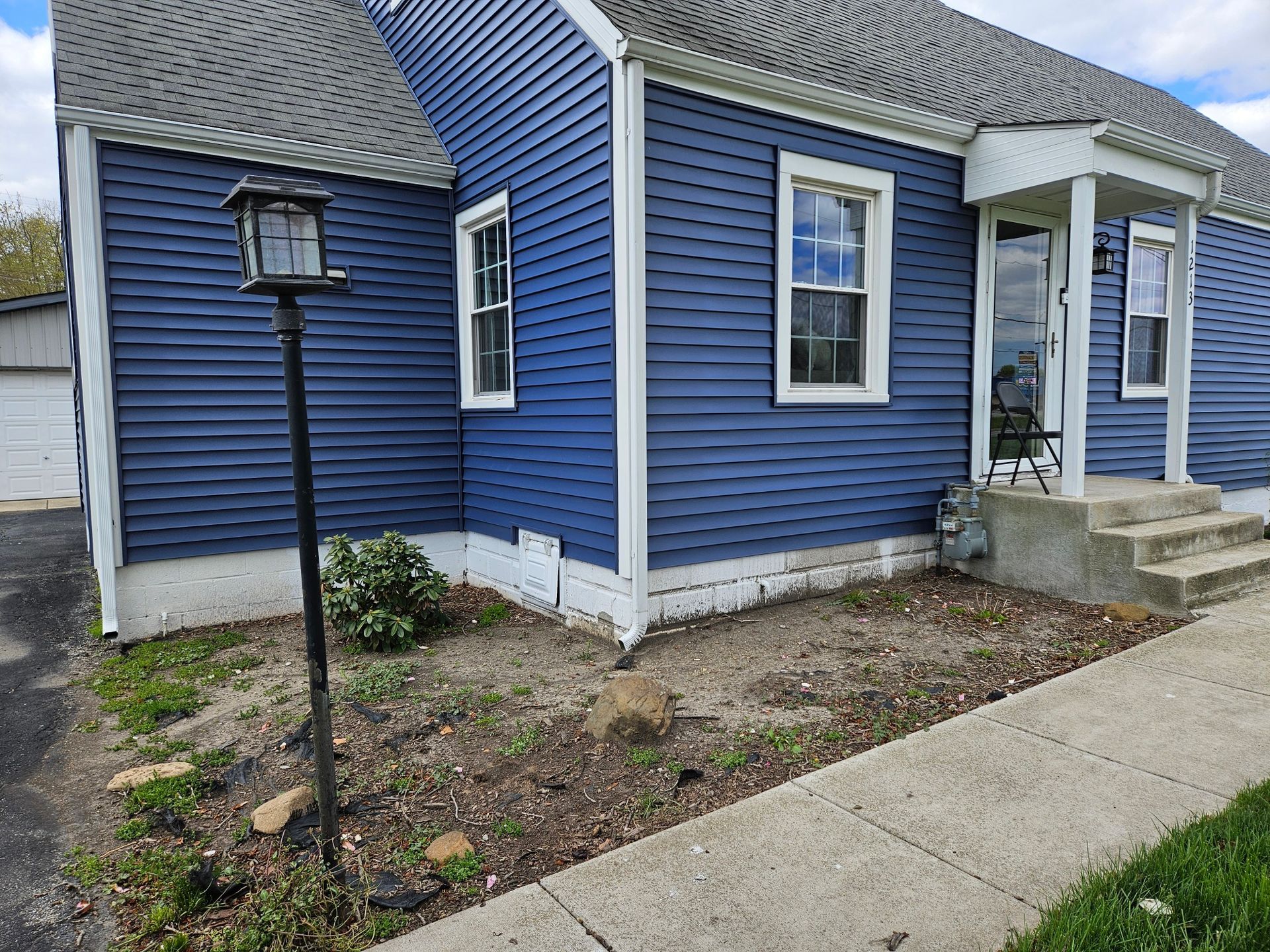 Front of a house with trimmed shrubs, a wooden porch, and a gravel path