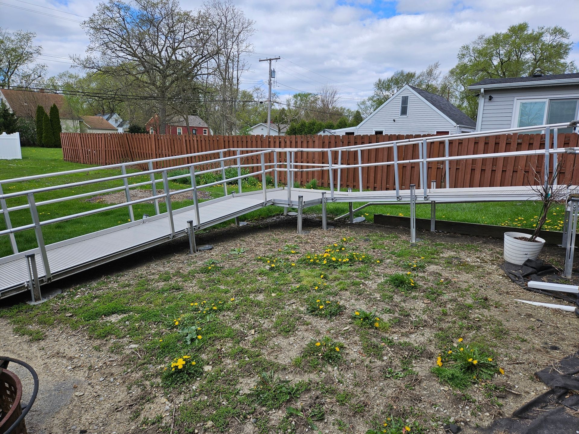 Backyard garden with raised ramp and white railing beside a wooden fence under a cloudy sky