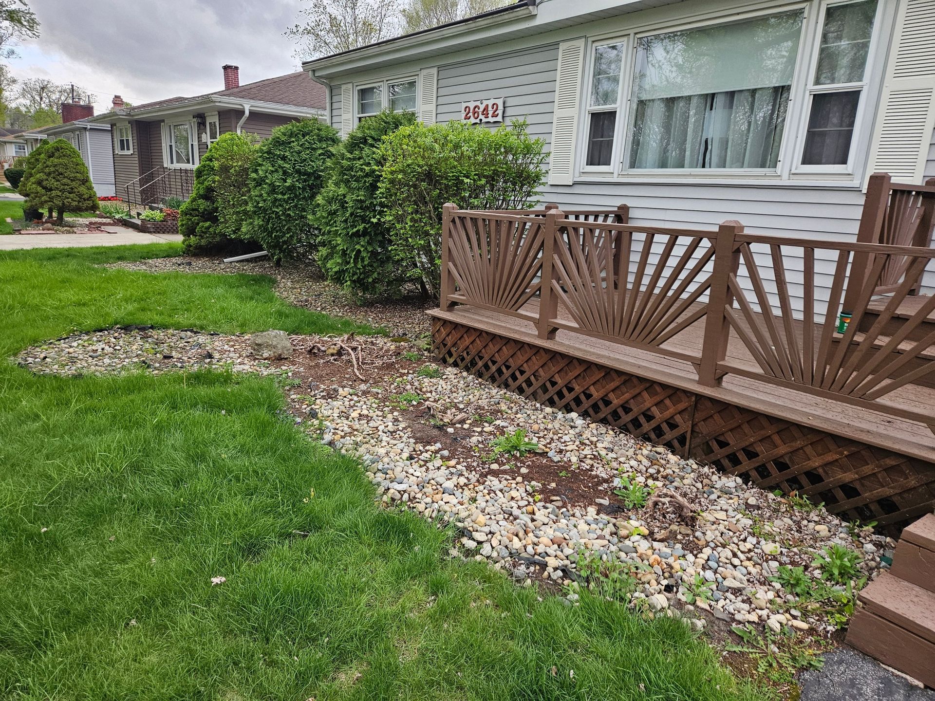 Backyard garden with raised ramp and white railing beside a wooden fence under a cloudy sky