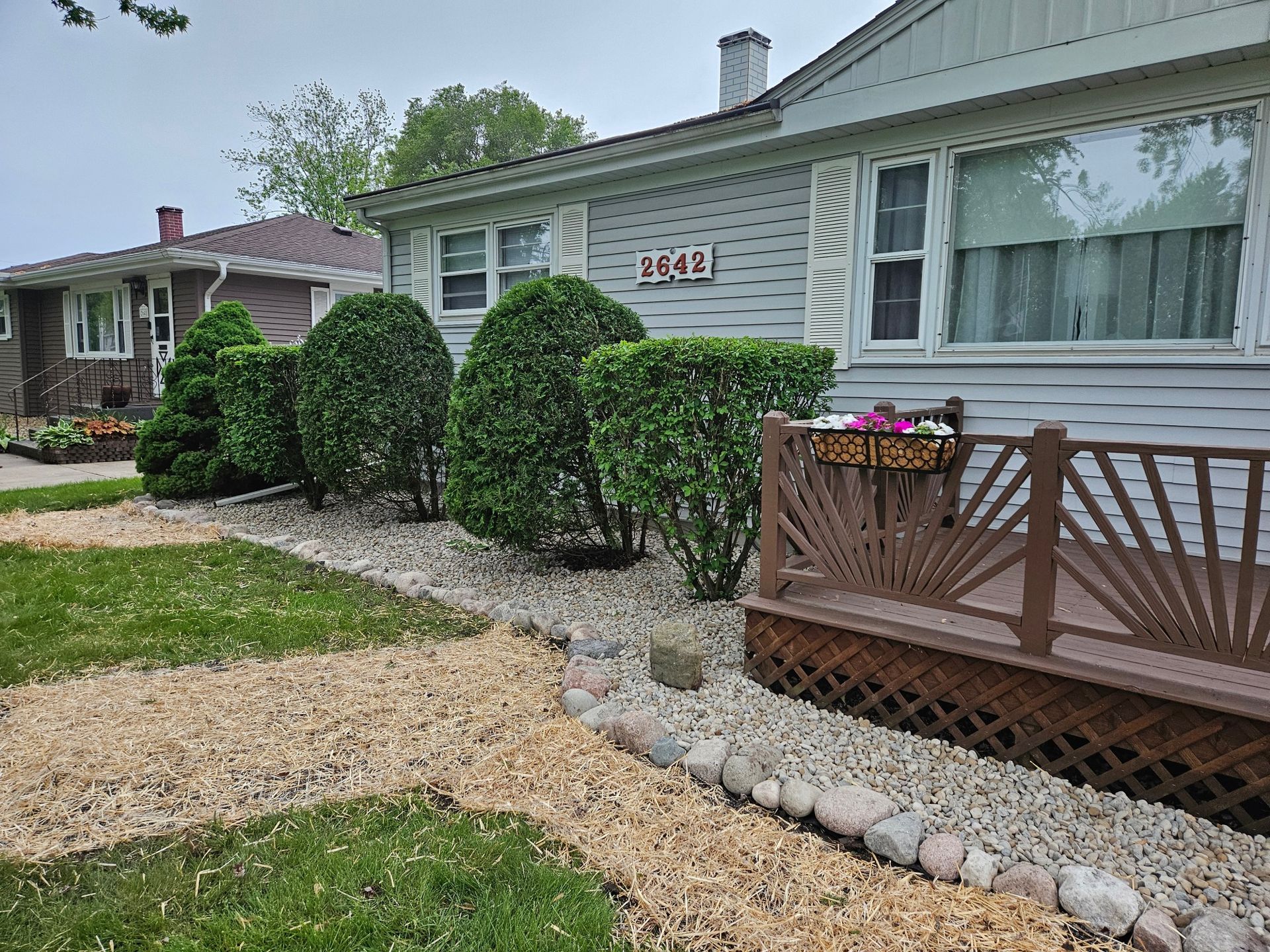 Front of a house with trimmed shrubs, a wooden porch, and a gravel path