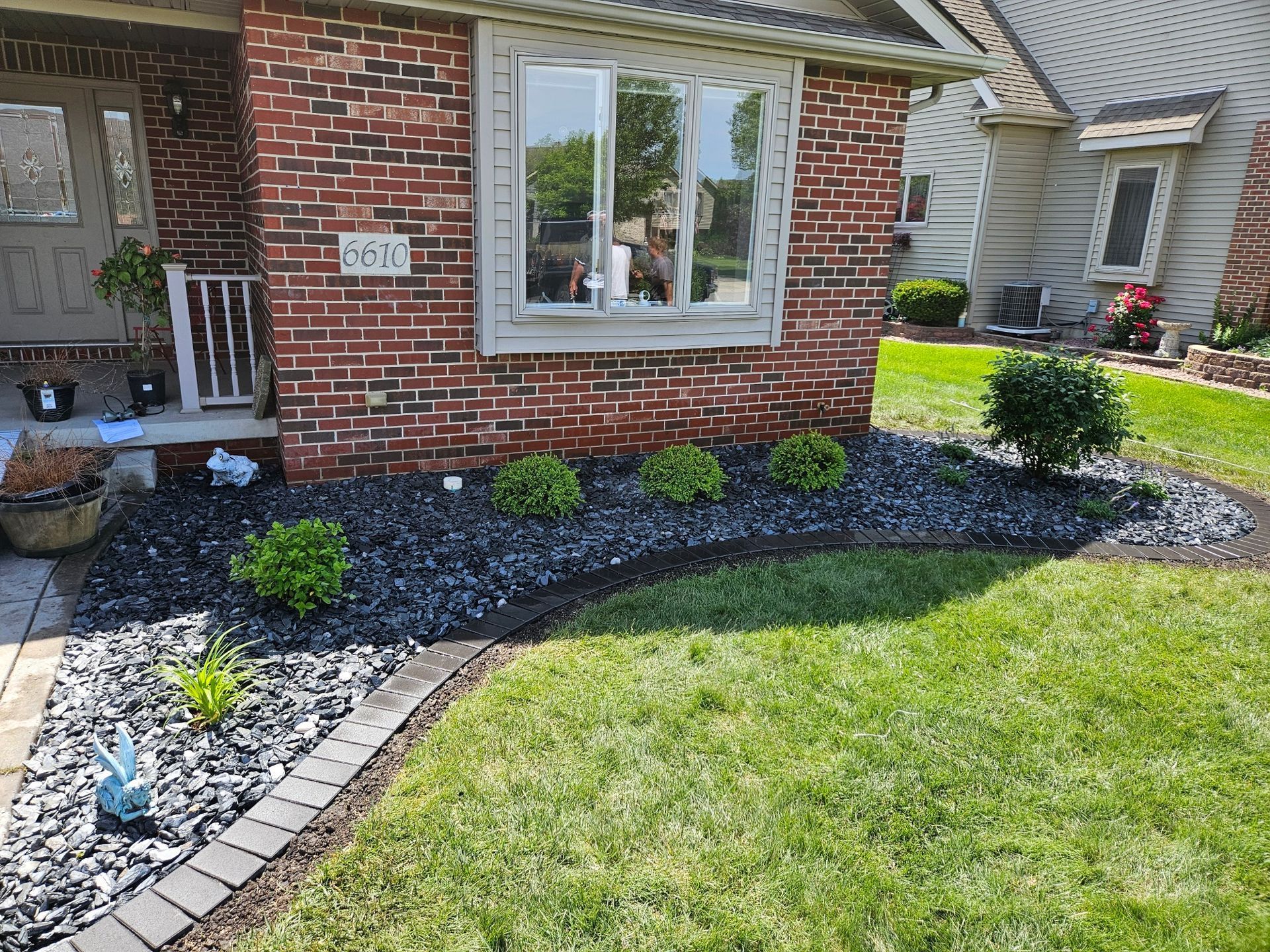 Brick house front yard with curved stone border, black mulch, shrubs, and green lawn.