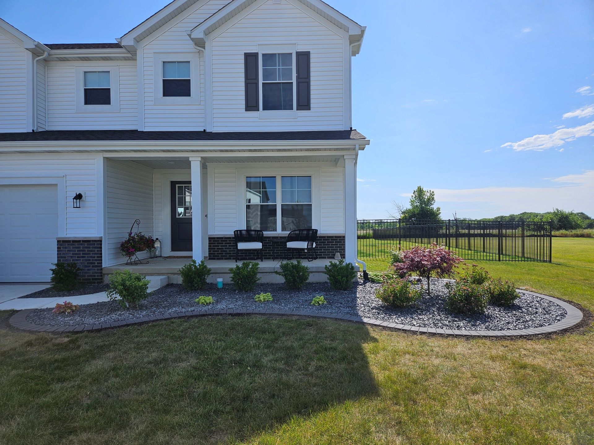 Two-story white house with a front porch, landscaped yard, and fenced backyard under a blue sky