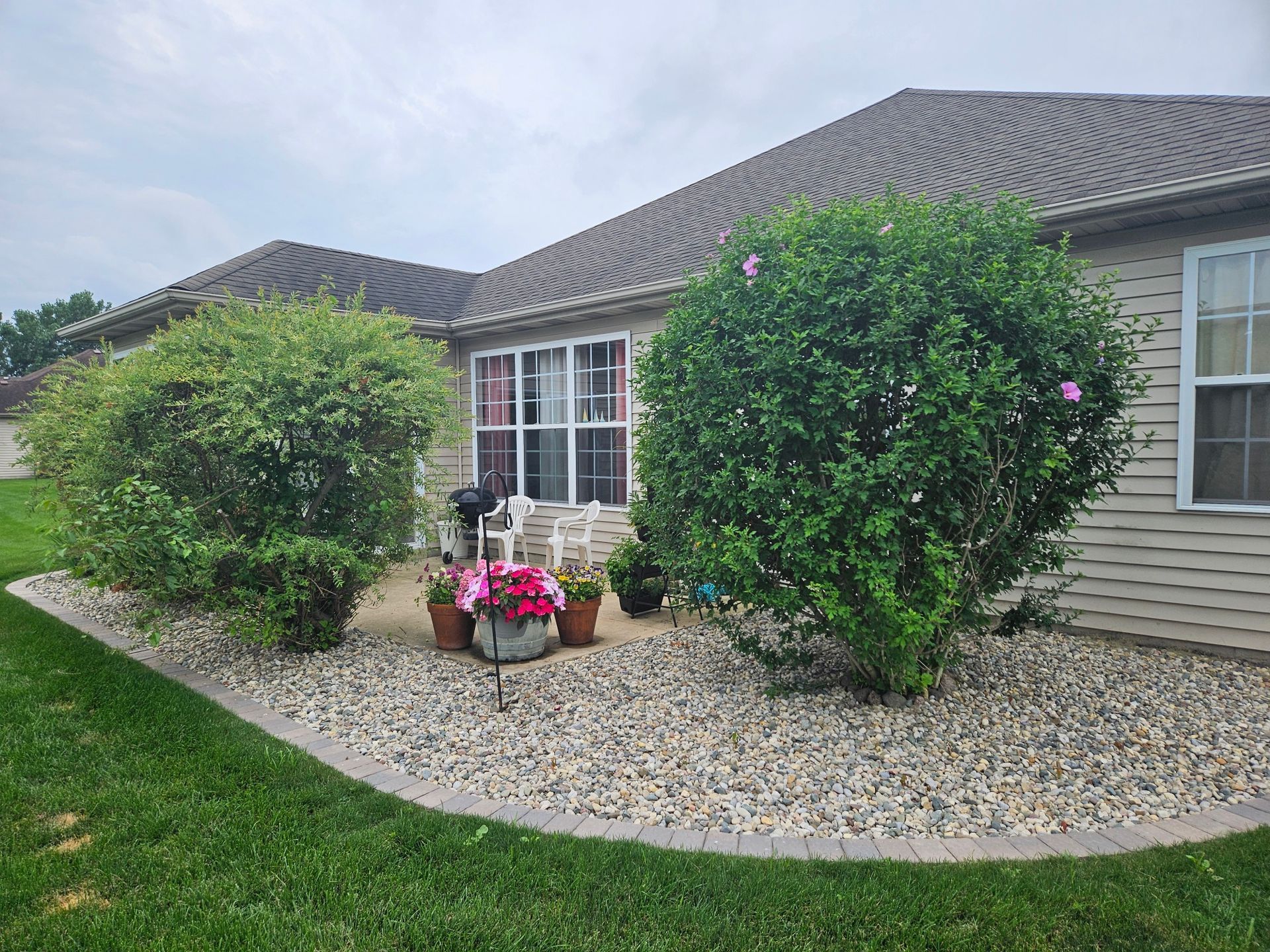 Front yard of a suburban house with white columns, stone facade, and landscaped garden in bright sunlight