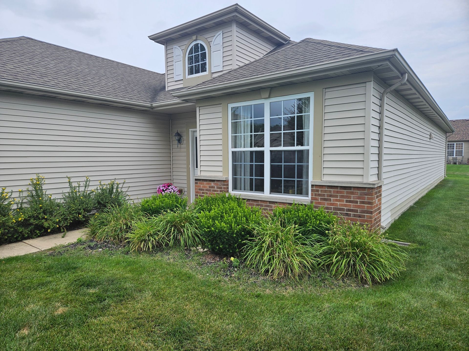 Curved stone garden bed beside a brick house with a walkway and lawn