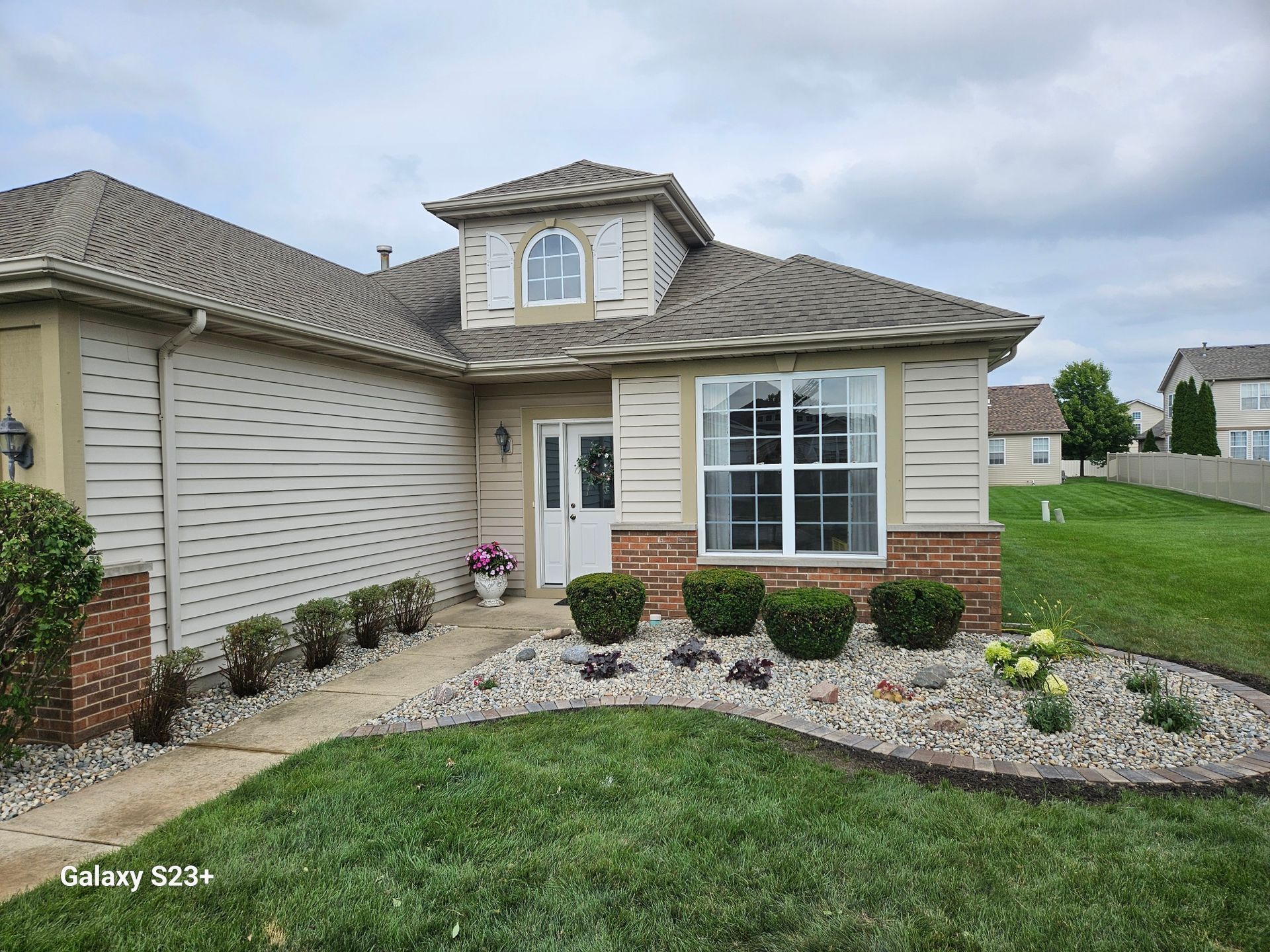 Suburban house exterior with beige siding, two-car garage, front windows, and landscaped lawn.