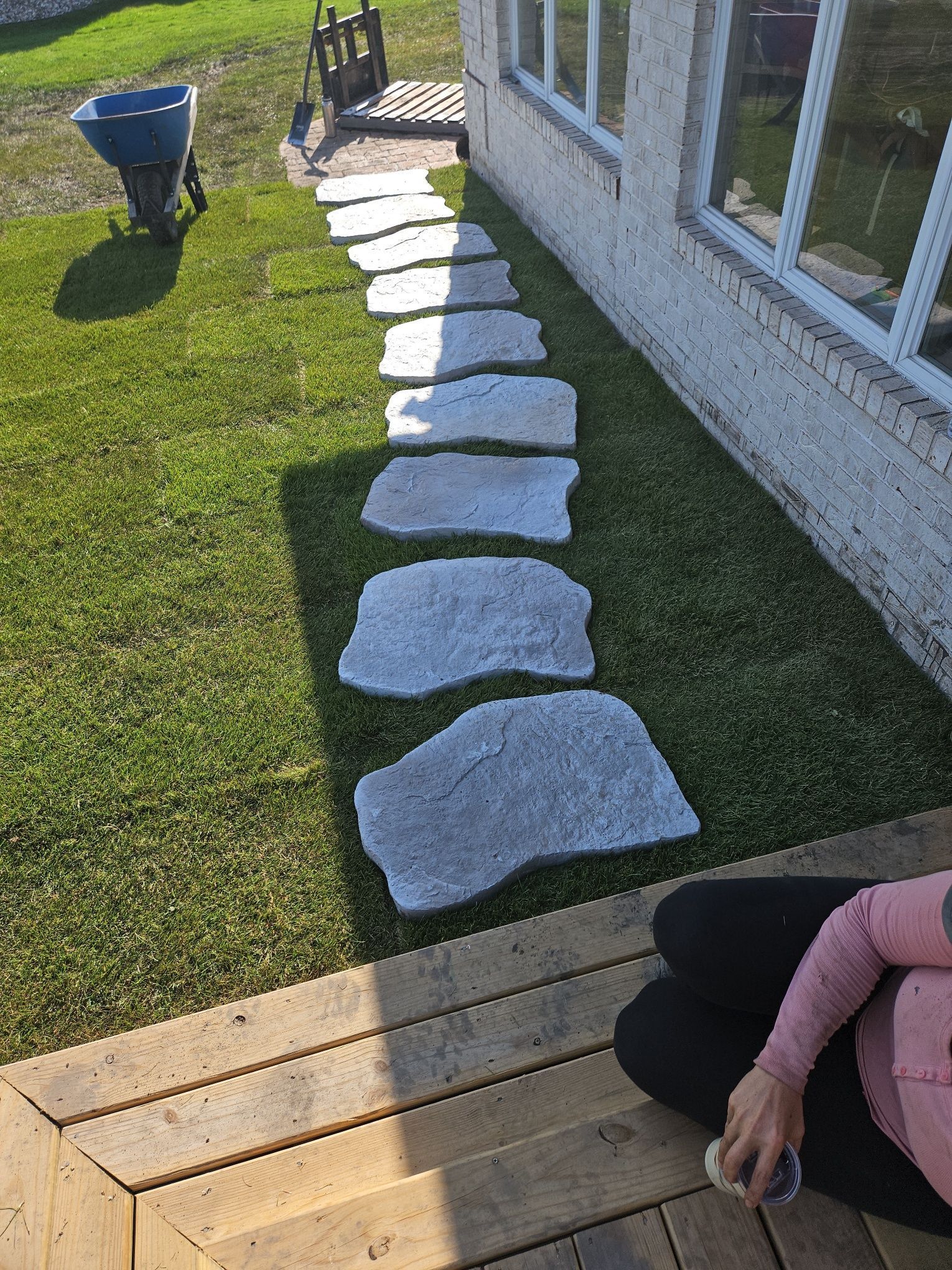 Stone stepping path across a lawn beside a house, leading from a wooden deck to a chair.