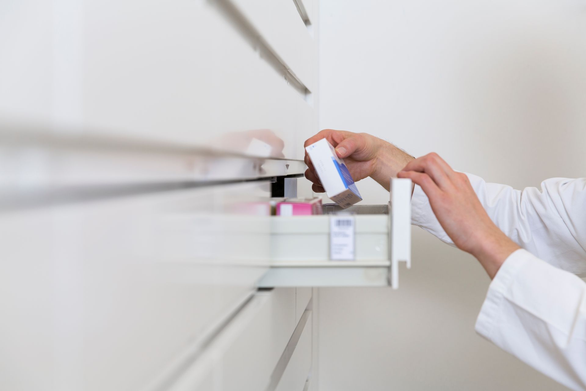 Una persona in camice bianco mette una scatola di medicinali in un cassetto di un armadietto.
