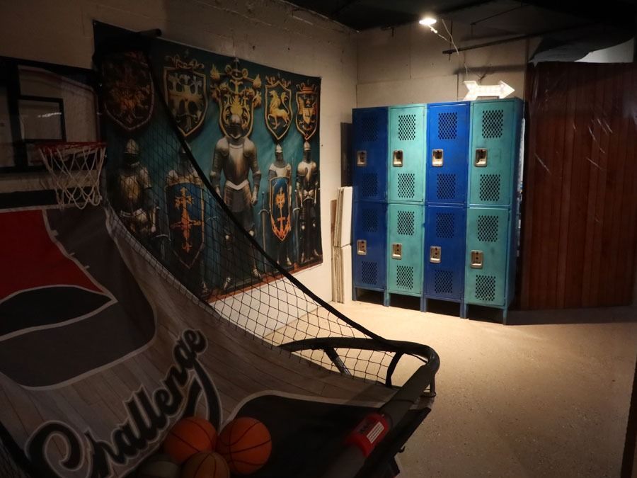 Basement rec room with arcade basketball game, blue lockers, sports posters, and a brown wooden cabinet