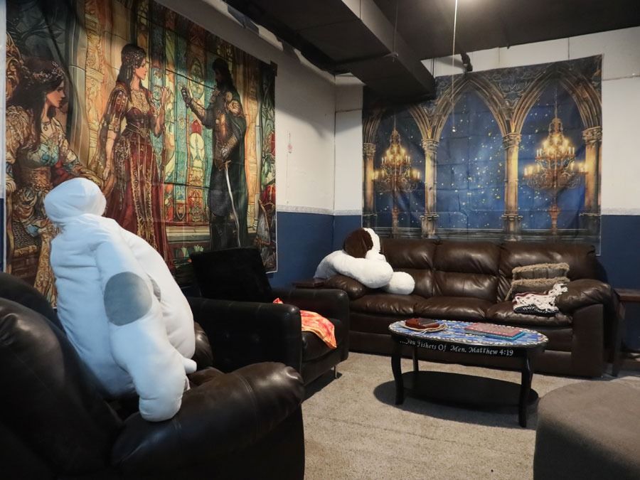Cozy basement lounge with two white plush gorilla chairs, brown leather couch, and fantasy wall tapestries.