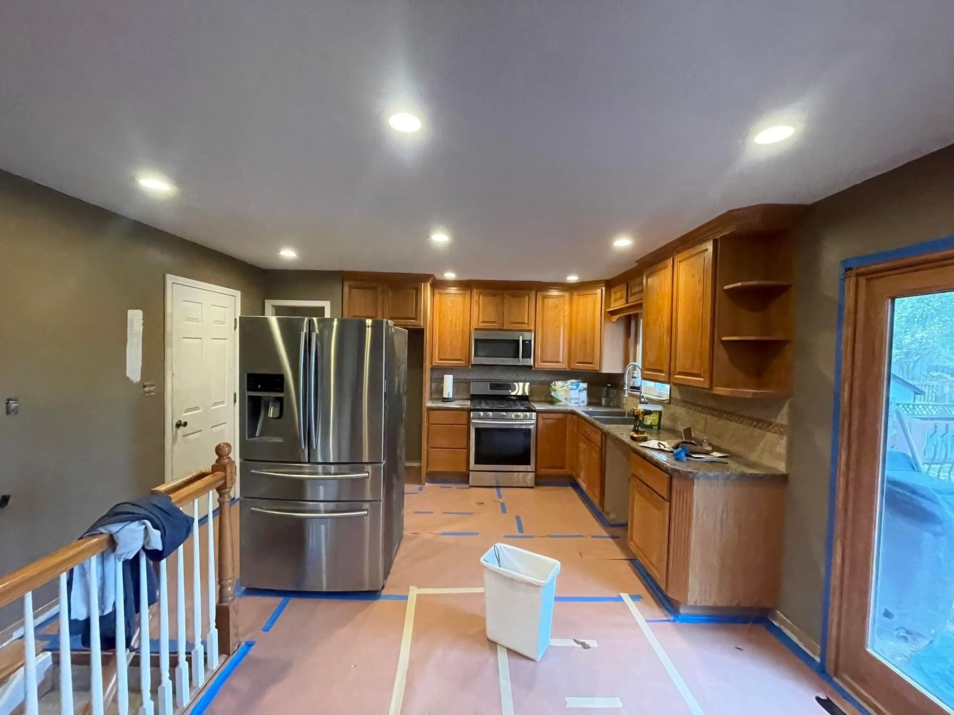 A kitchen with stainless steel appliances and wooden cabinets is being painted.