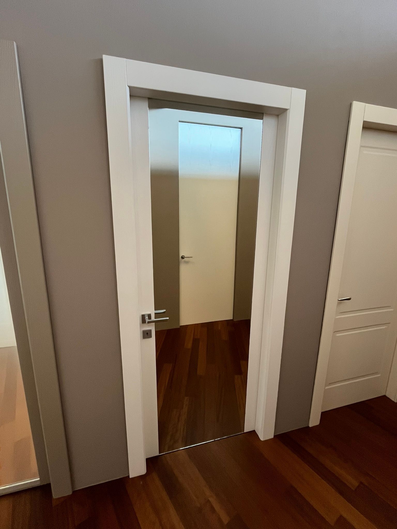 Porta aperta con cornice bianca in una stanza moderna con pavimento in legno e pareti grigie.