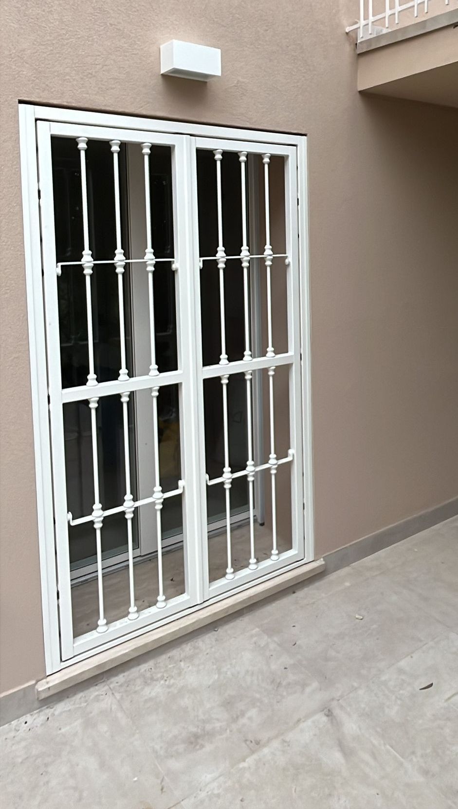 Porta con sbarre bianche su una parete esterna beige accanto a un vialetto in cemento.