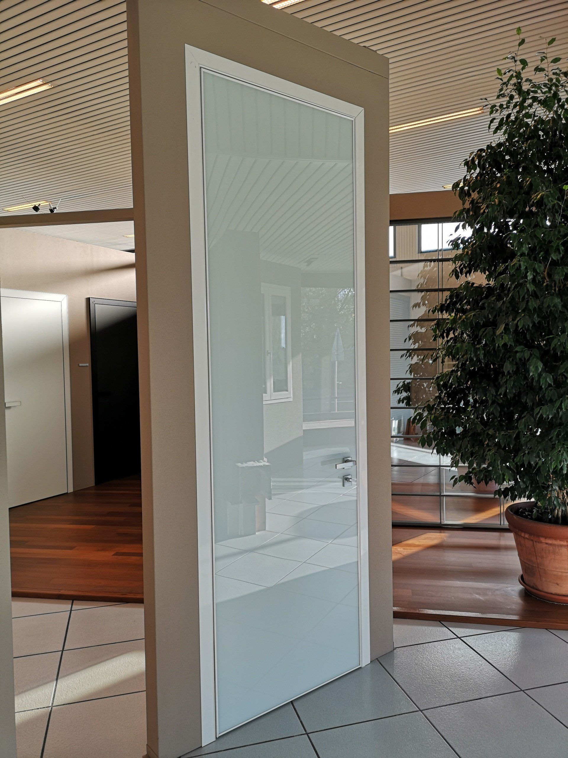 Porta a vetri in una hall moderna con soffitto decorato, pavimento piastrellato e albero in vaso nelle vicinanze.