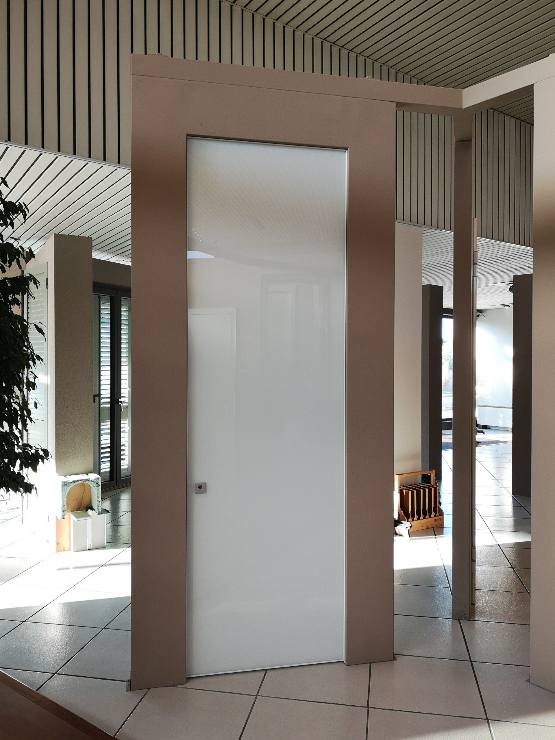 Porta bianca in una parete divisoria con cornice rosa all'interno di un luminoso interno moderno con pareti a righe e pavimento piastrellato.
