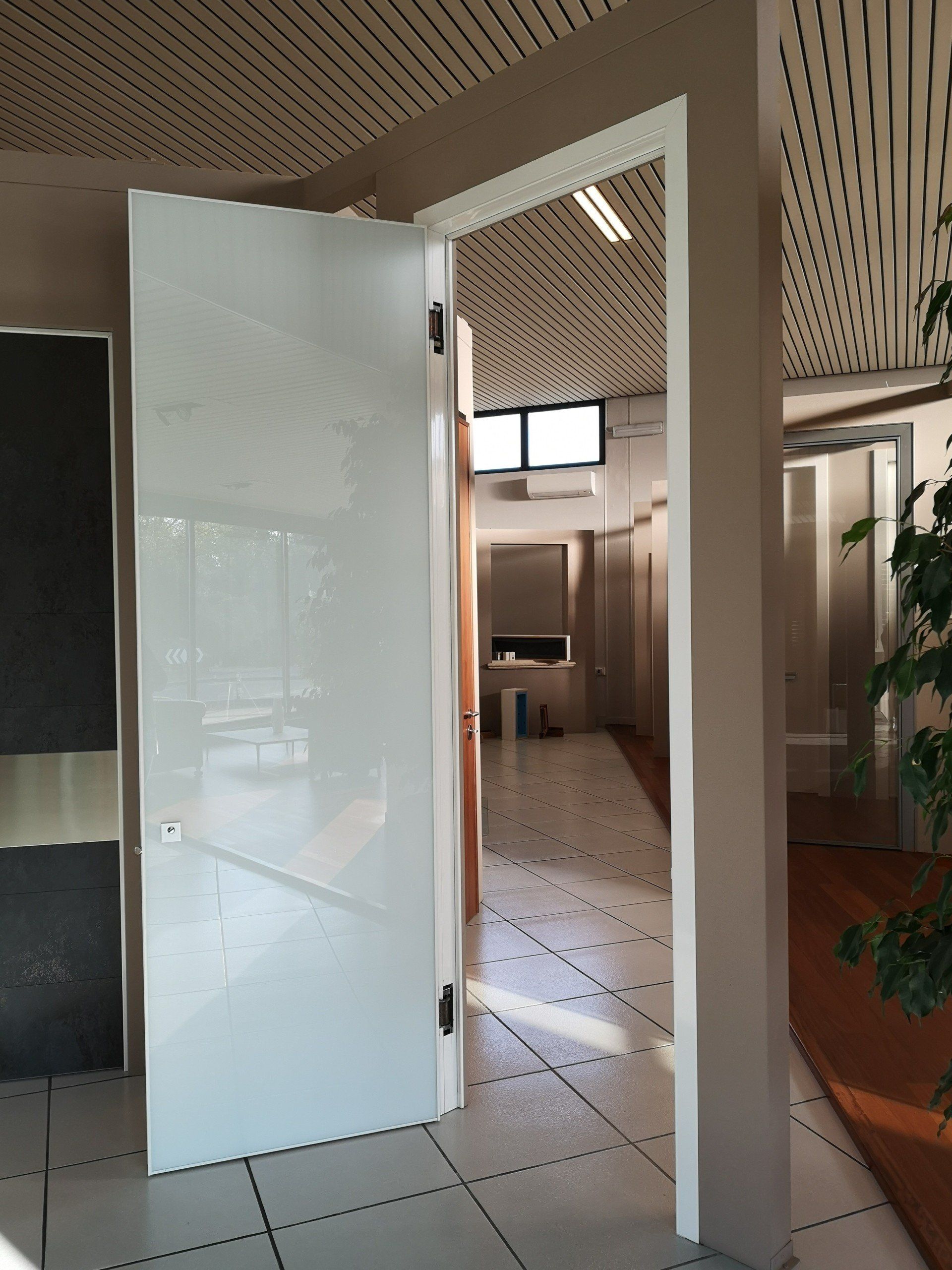Apri una porta bianca che conduce a un luminoso corridoio interno con soffitto decorato e pavimento piastrellato.