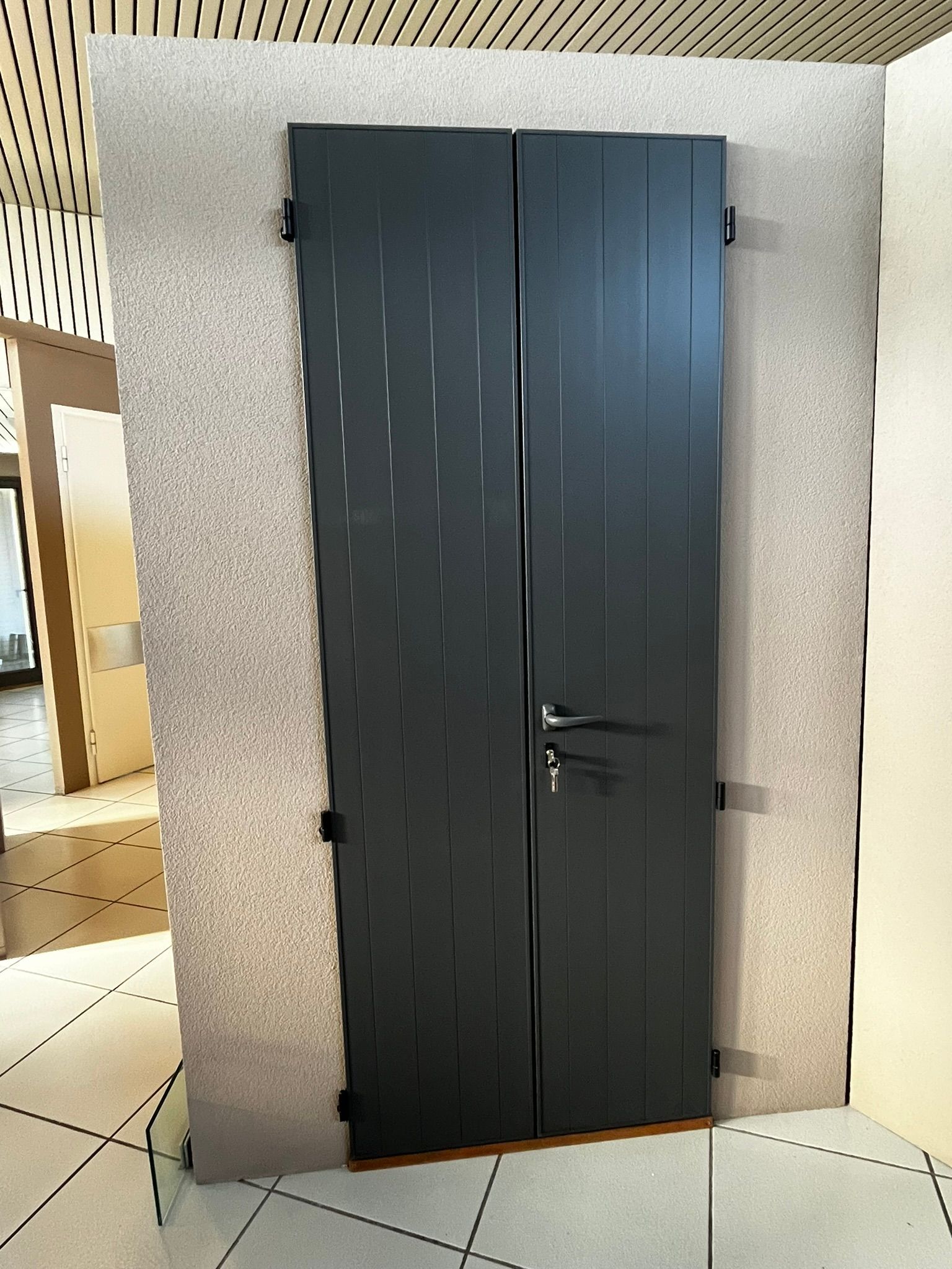 Pannello espositivo scuro a doppia anta montato su una parete screziata in uno showroom.