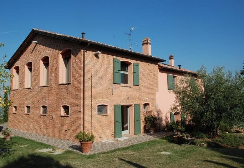 Casa rosa a due piani con persiane verdi e giardino sotto un cielo azzurro limpido