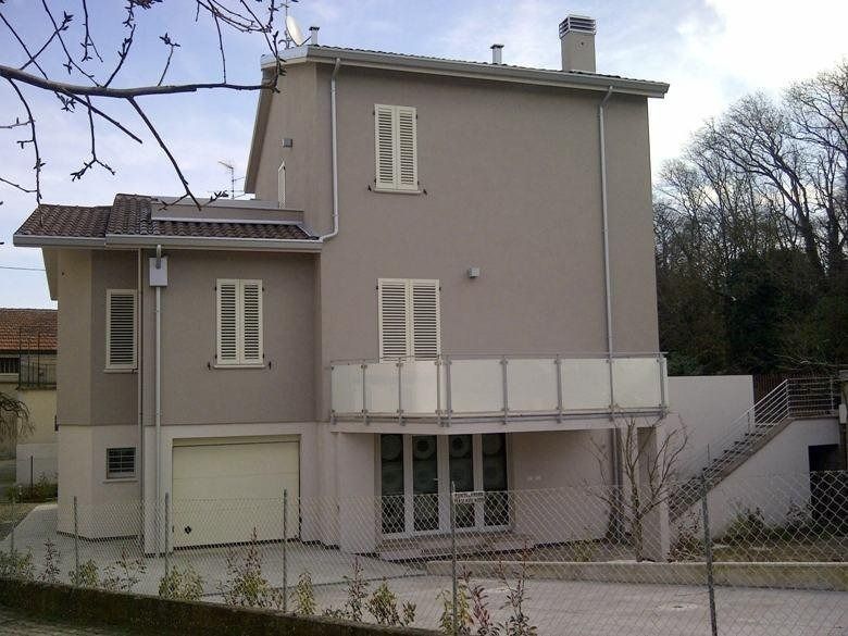 Casa beige a due piani con garage, balcone e scala esterna in una zona residenziale.