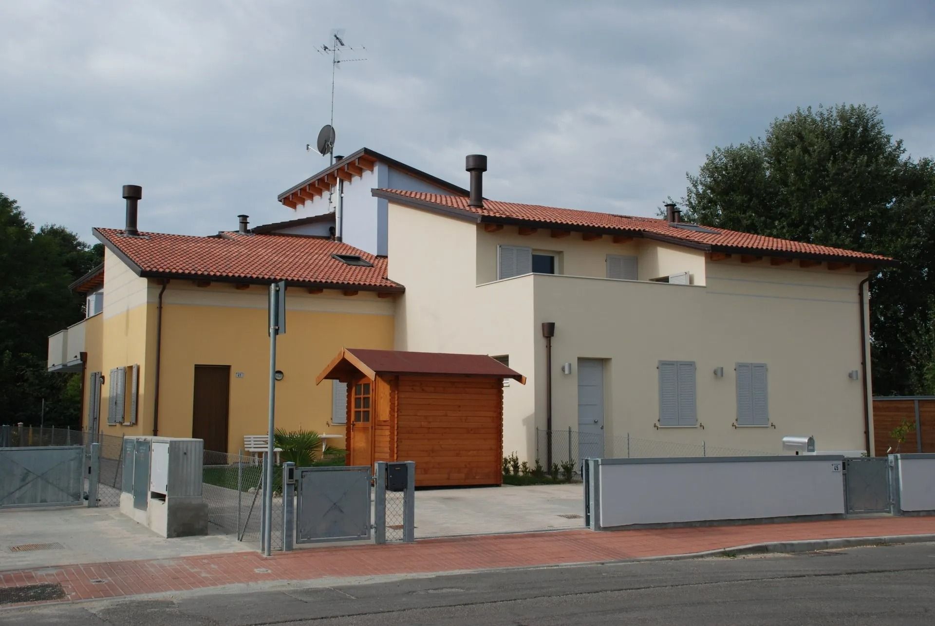 Casa beige a due piani con tetto di tegole rosse e piccolo cancello d'ingresso su una strada