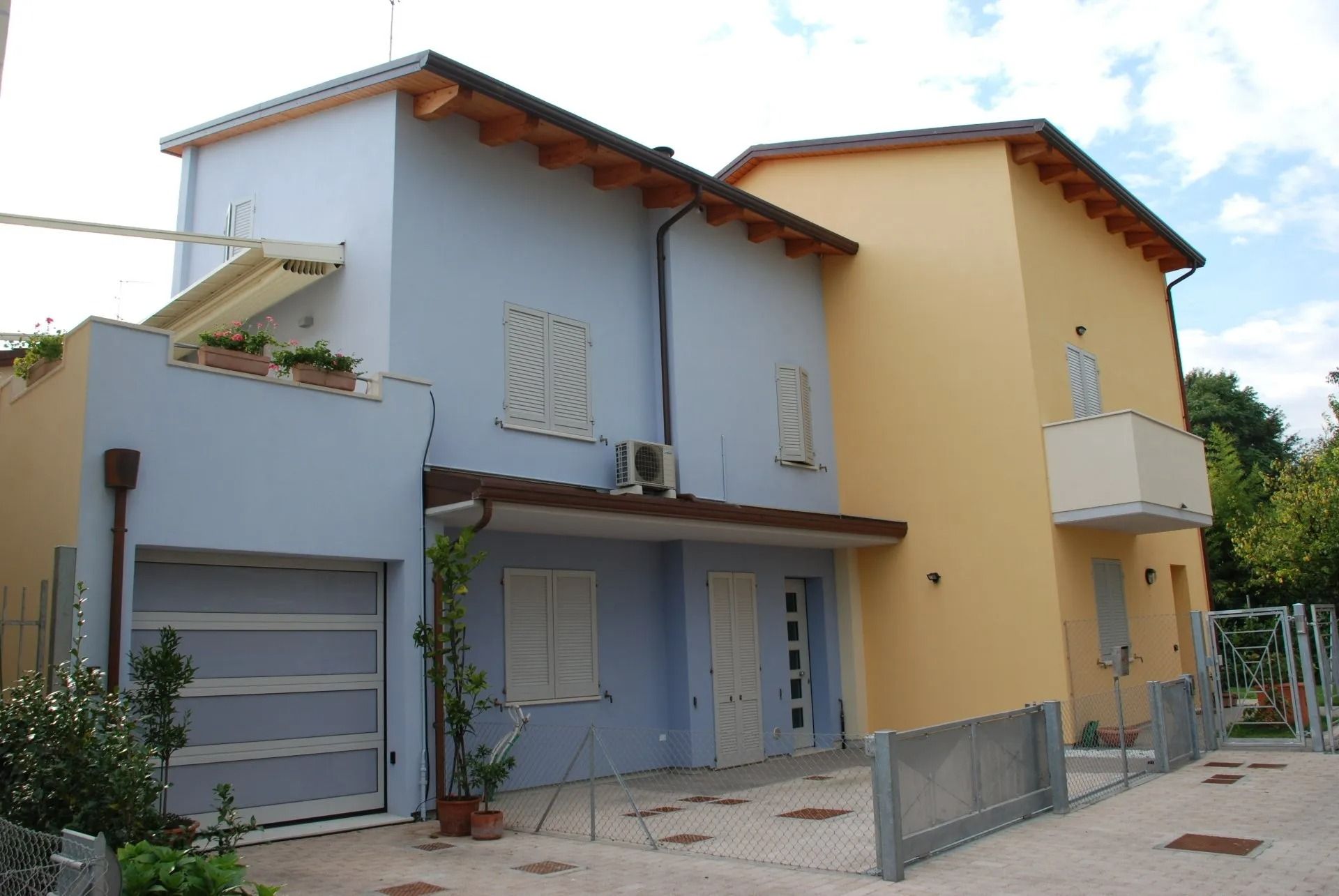 Due case colorate a schiera, una bianca e blu, l'altra gialla, con porte da garage e un piccolo vialetto d'accesso.