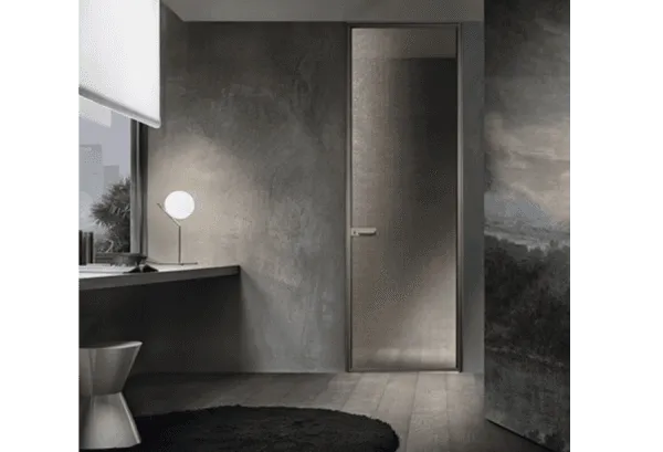Bagno minimalista grigio con lavabo, lampada da specchio accesa e porta in vetro satinato.