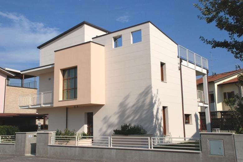 Casa moderna a due piani di colore beige con cortile recintato sotto un cielo azzurro limpido.
