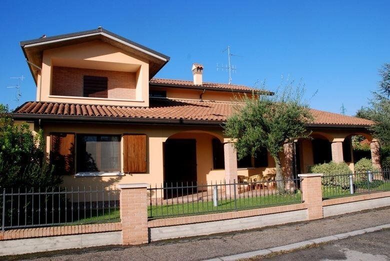 Casa a due piani color pesca con tetto di tegole e portico anteriore dietro una bassa recinzione in una strada soleggiata