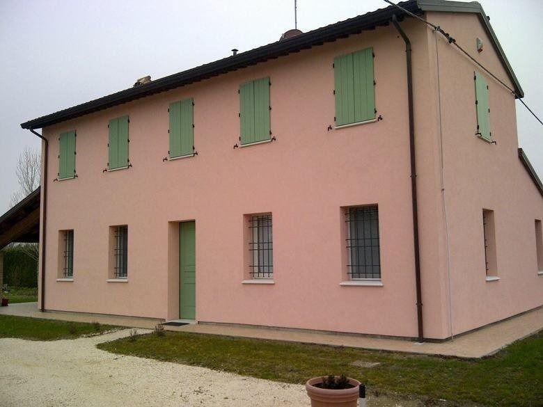 Casa rosa a due piani con persiane verdi e un piccolo cortile