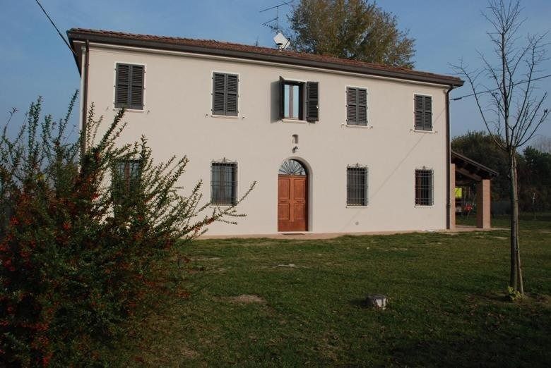 Casa a due piani color crema con persiane grigie e porta ad arco marrone su un prato erboso