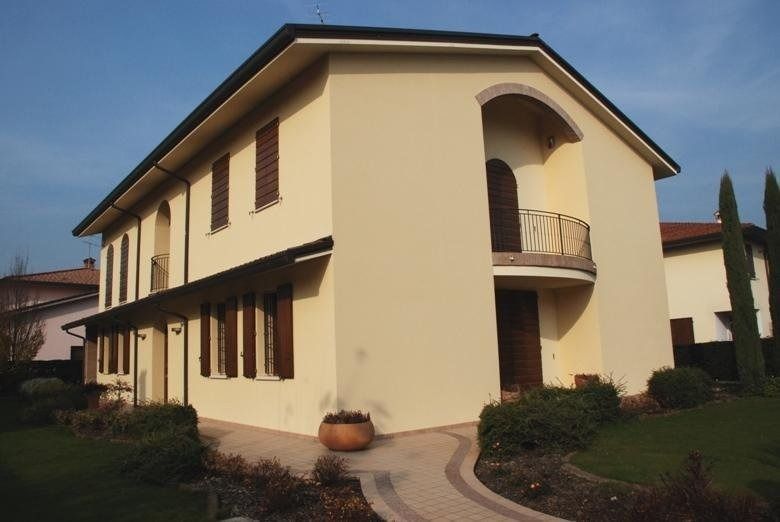Casa beige a due piani con balcone ad arco, finiture marroni e passerella curva sul davanti.