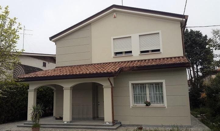 Casa a due piani di colore beige con tetto in tegole rosse e portico anteriore coperto, situata in una strada tranquilla.