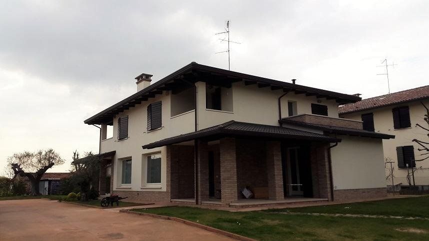 Casa a due piani color beige con tetto scuro e portico in mattoni, situata in una tranquilla strada di periferia.