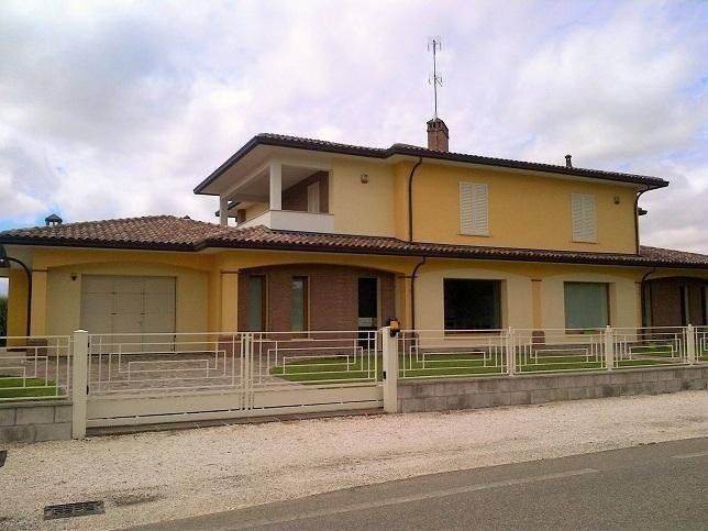 Casa gialla a due piani con tetto di tegole e recinzione anteriore, situata accanto a una strada.