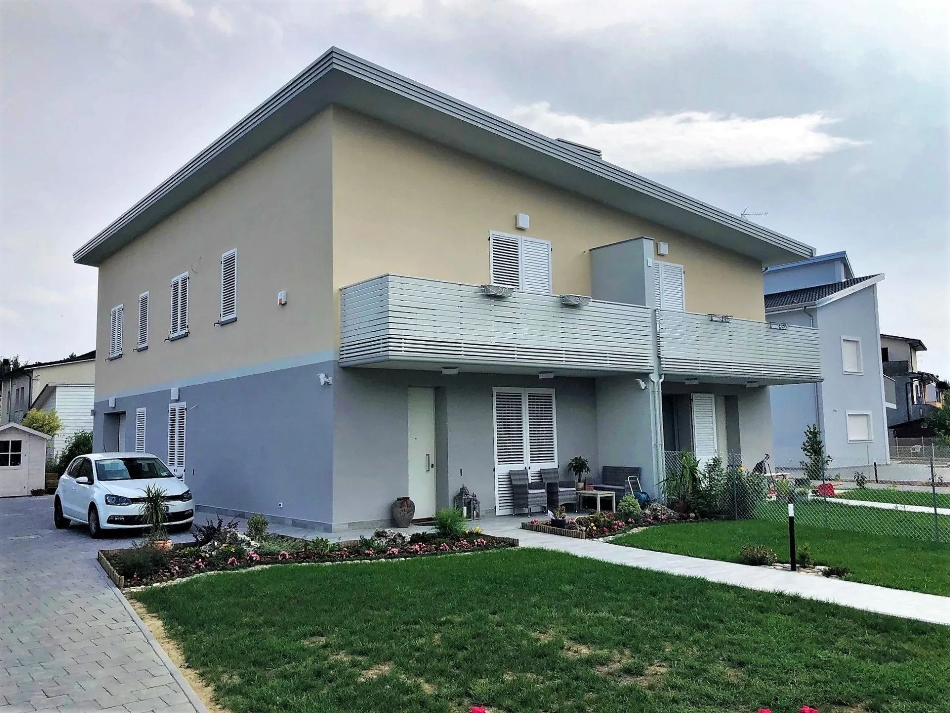 Casa a due piani con prato verde, vialetto d'accesso e auto parcheggiata sotto un cielo nuvoloso.