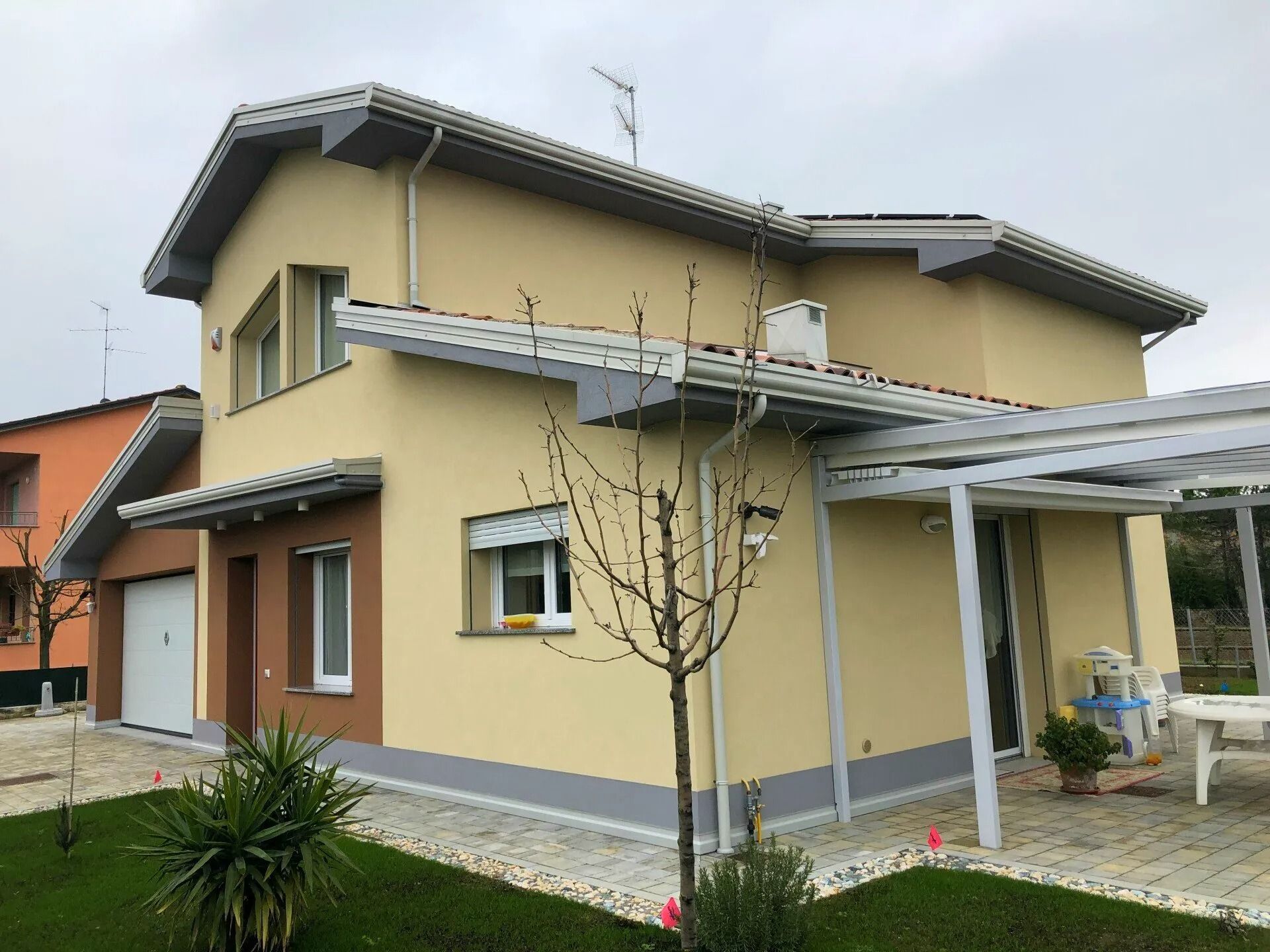 Casa moderna a due piani di colore beige con tetto grigio, finiture bianche e un piccolo giardino anteriore.