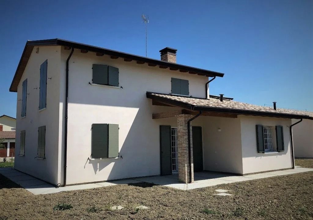 Casa bianca a due piani con persiane grigie e tetto di tegole sotto un cielo azzurro limpido.