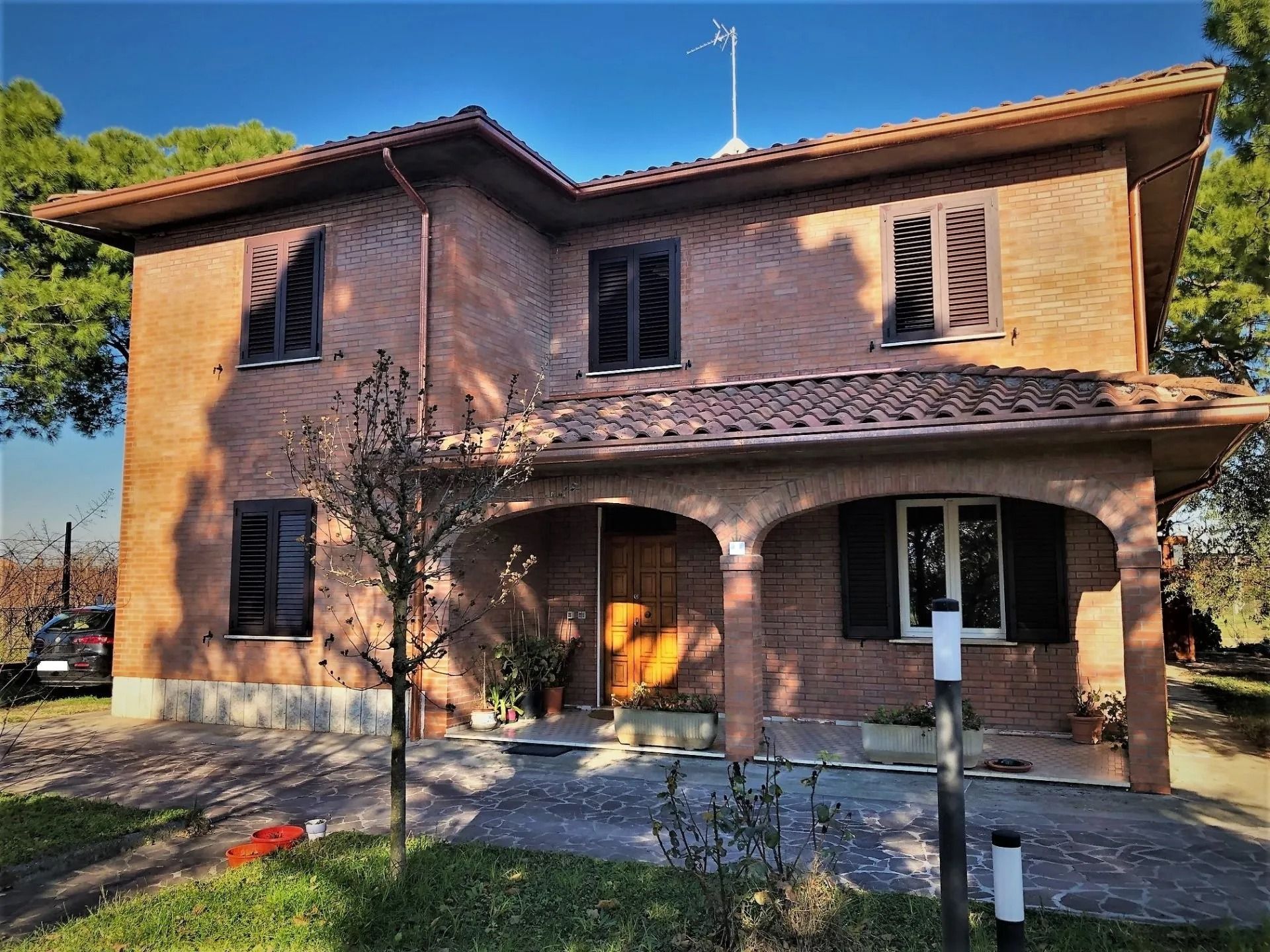 Casa a due piani in mattoni con portico piastrellato e giardino anteriore soleggiato