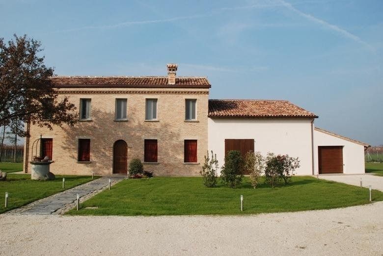 Casale in pietra con tetto in terracotta, persiane rosse e un prato verde sotto un cielo limpido