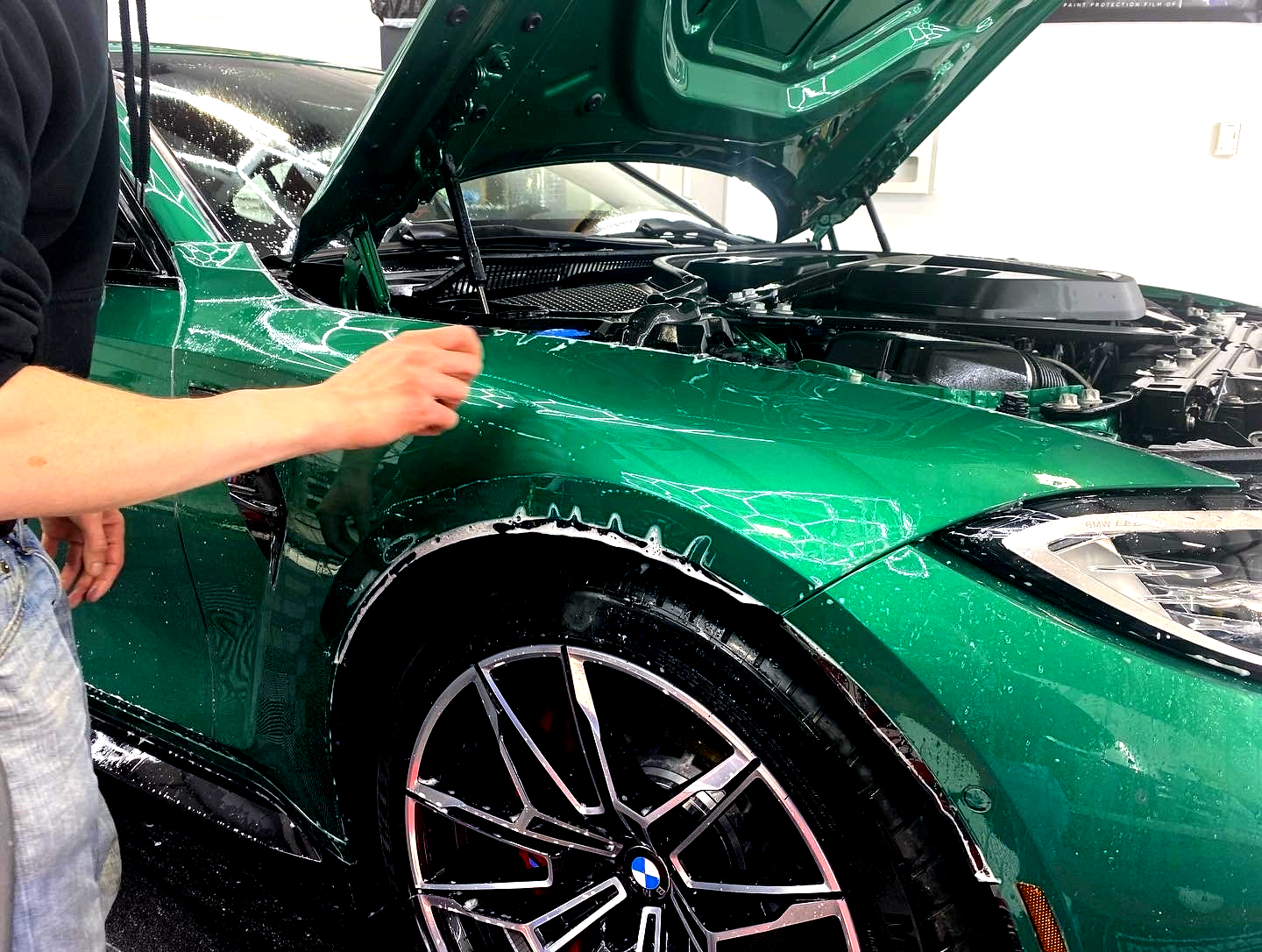 Person washing a bright green BMW with soapy water; hood open.
