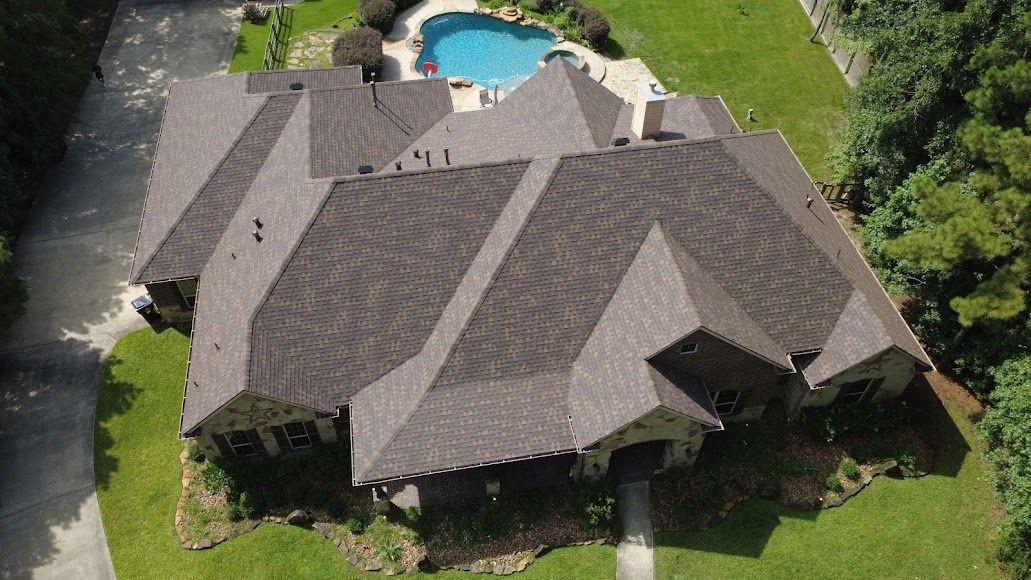 Aerial view of a large gray-roofed house with a backyard pool and green lawn.