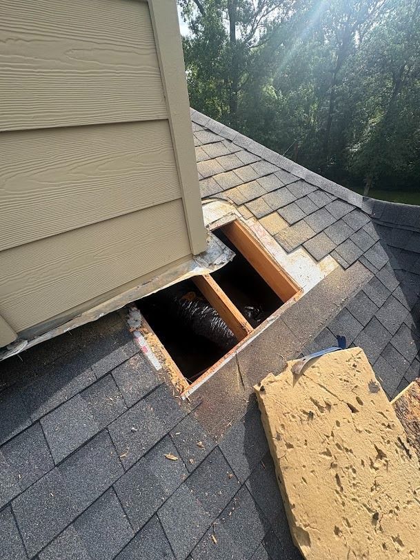 Roof with missing shingles and exposed opening near a wall, with debris on the sloped roof.