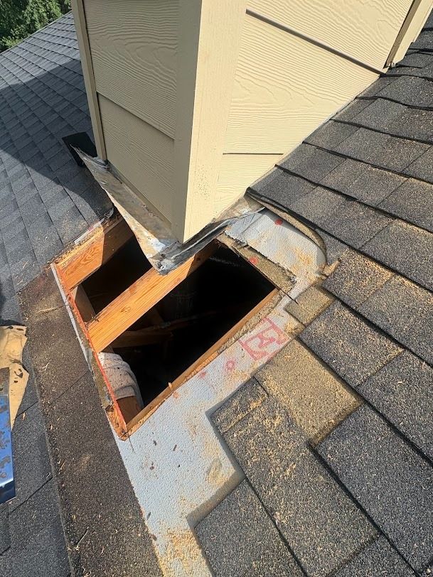 Damaged roof around a chimney with a large open hole exposing the attic below