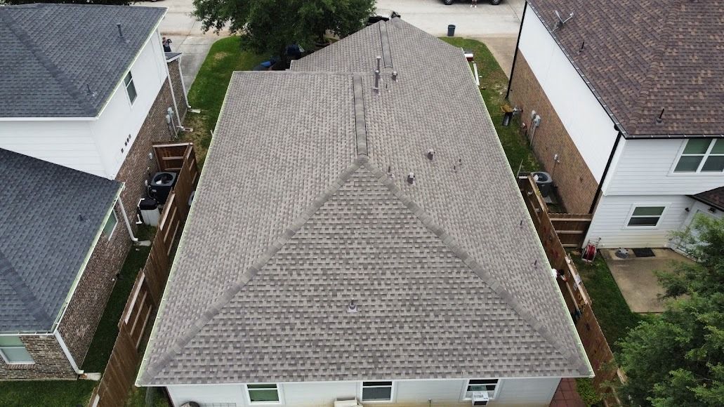 Aerial view of a gray shingled suburban house roof between two neighboring homes.