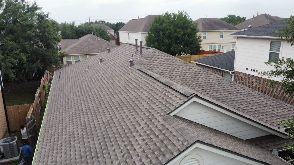 Rooftop with gray shingles and skylights in a suburban neighborhood on a cloudy day
