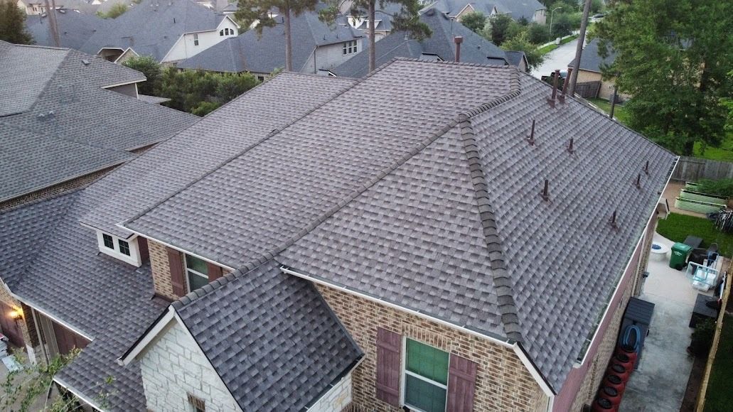 Aerial view of suburban houses with gray shingle roofs and a driveway between homes