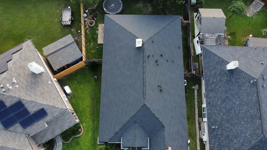 Aerial view of three rooftops, including a dark gray house centered between two smaller homes and a yard with solar panels.