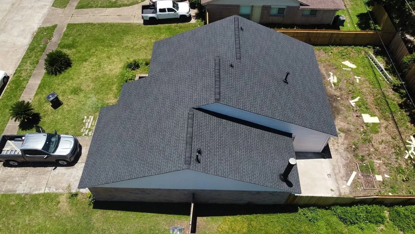 Aerial view of a dark gray house roof with a yard and parked vehicles around it.
